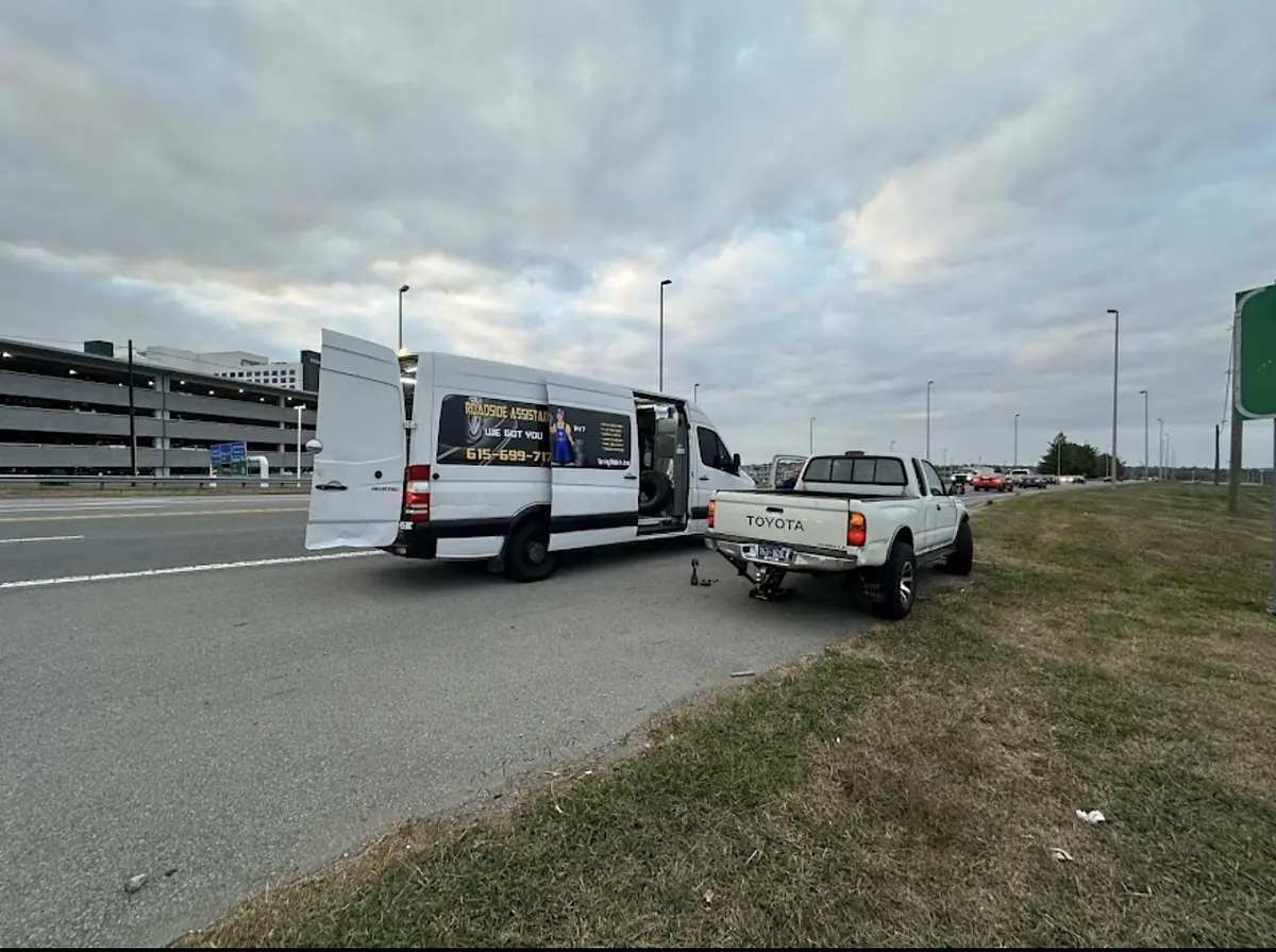 Service van parked behind a pickup on the highway shoulder while the crew changes a tire