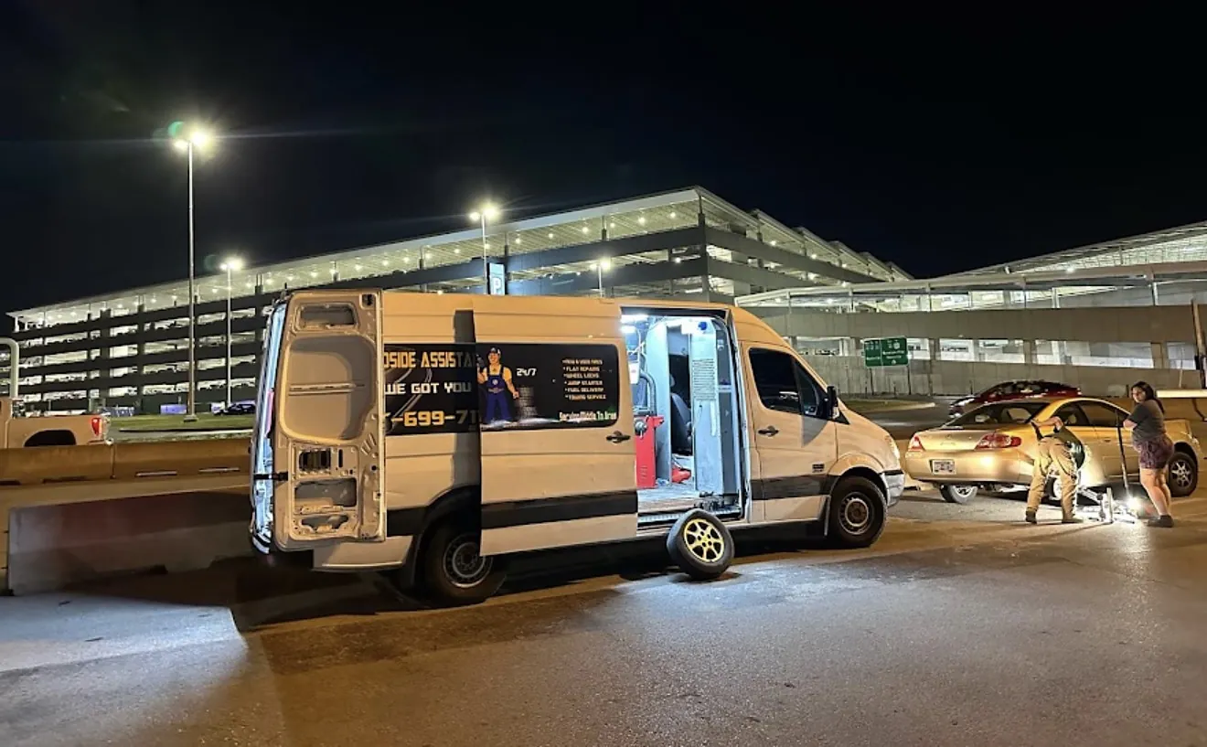Mobile Tire Solutions van with the side door open, crew fixing a driver's flat tire at night